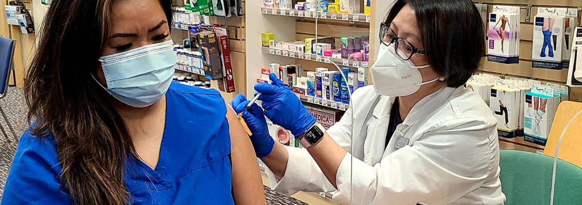 health worker in blue scrubs receiving vaccination by a pharmacist