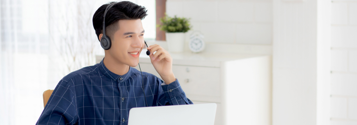 asian man wearing headset sitting in front of a laptop