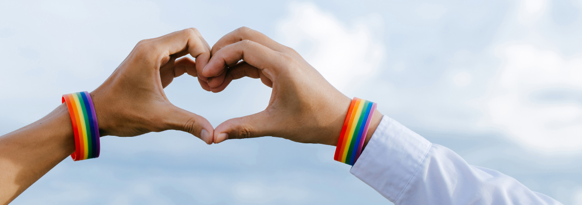 two hands making a heart wearing pride flag bracelets