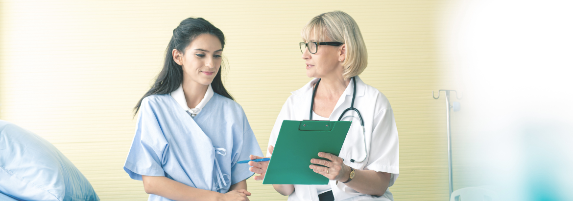 female patient dressed in hospital gown talking with her health care provider 