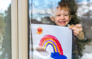 young boy inside holding picture of a rainbow
