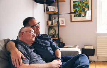 A male couple sitting embraced on a couch in a living room setting