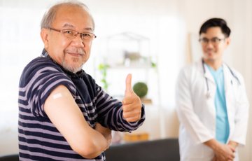 person smiling with bandaid on arm and doctor in background