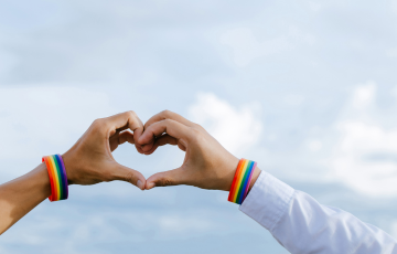 two hands making a heart wearing pride flag bracelets