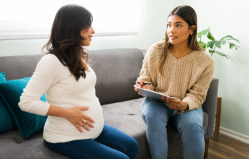 Midwife and pregnant patient talking on a couch