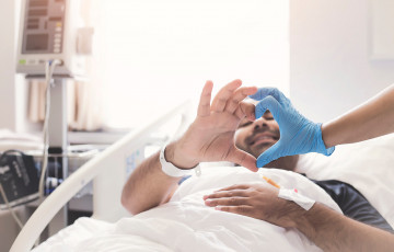 Man in hospital bed making heart shape with his hands and that of a care provider