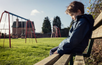 a young boy sitting on a park bench alone