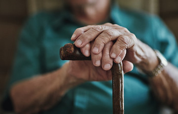 older figure with hands on a cane