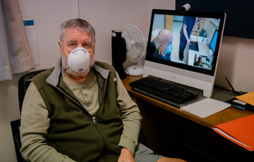 Alan Holt siting in front of a computer screen wearing a medical mask